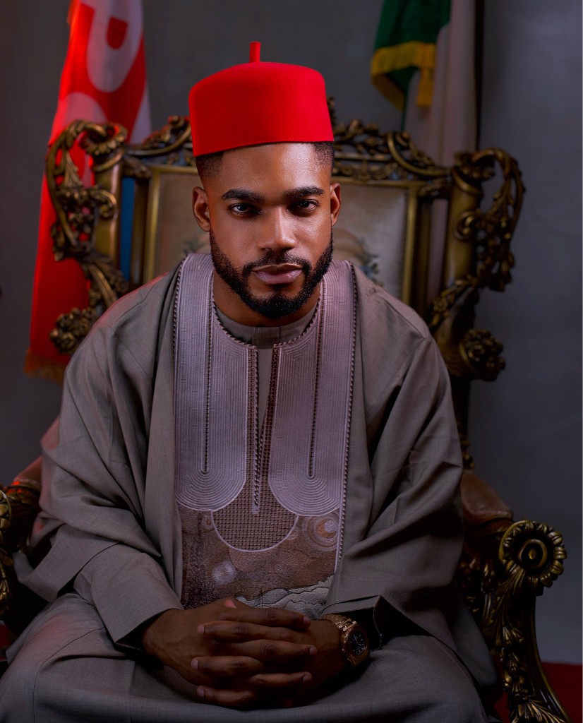 Osborn Nweze Umahi seated in a taupe agbada and red cap, hands clasped.