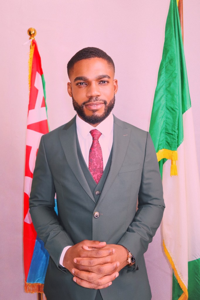 Osborn Nweze Umahi standing in a green suit, hands clasped, with flags behind him.